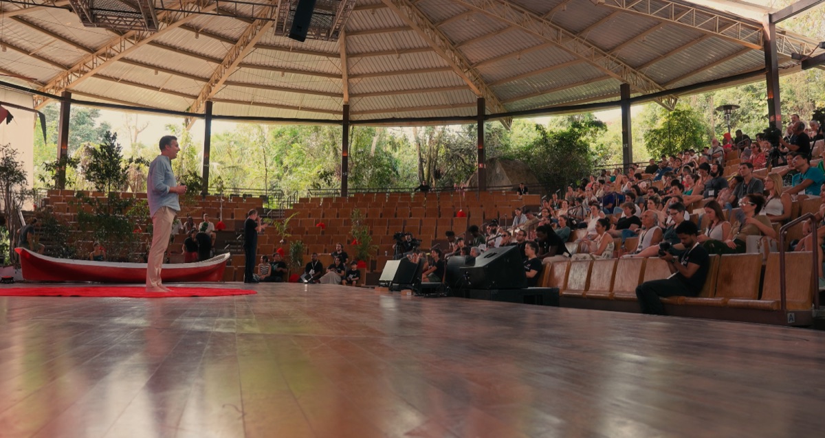 Palestrante com canoa caiçara no palco do TEDx Ilhabela, plateia cheia